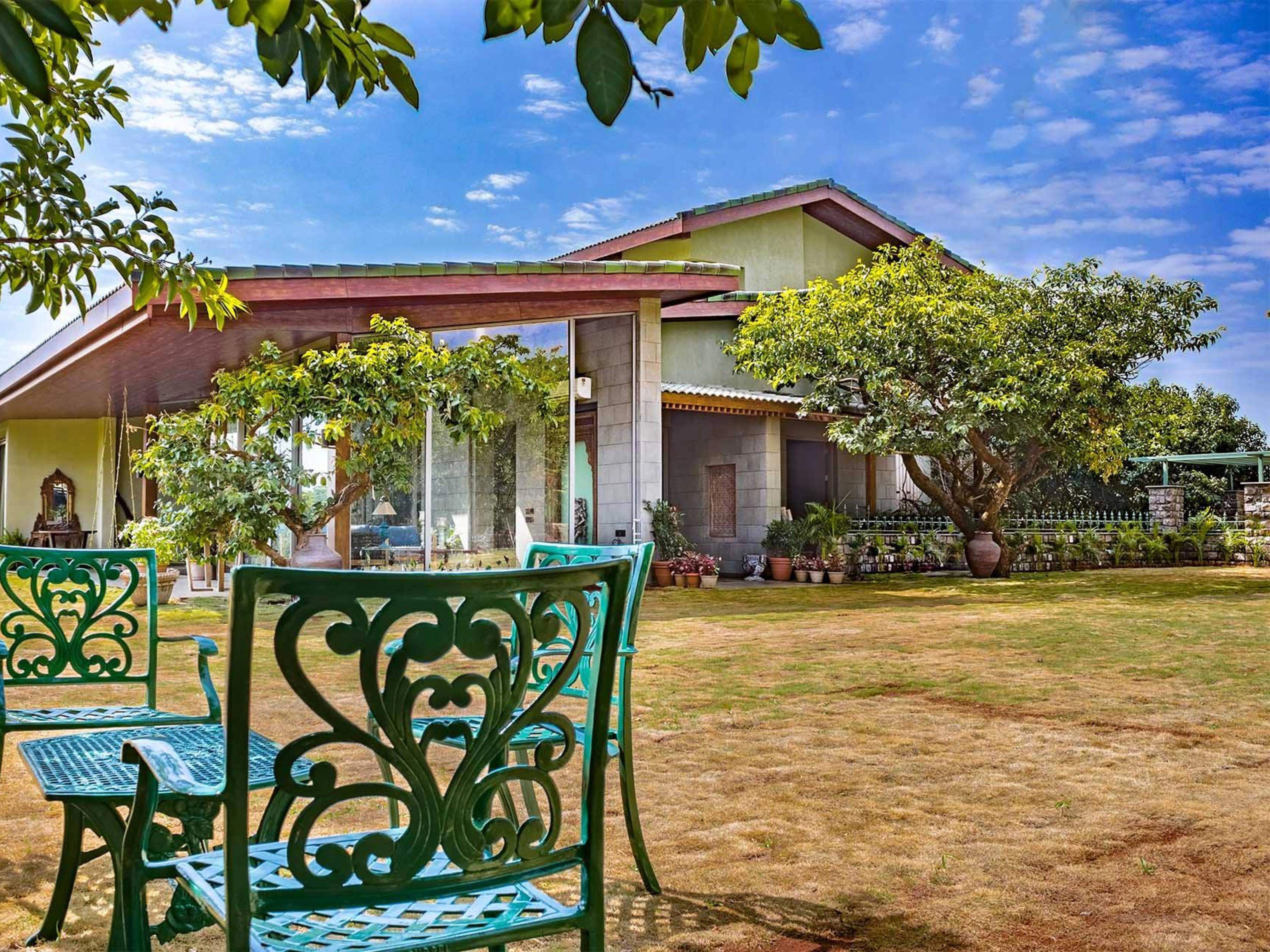 A two-story modern house with large glass doors and a spacious green lawn, set against a backdrop of hills under a clear sky